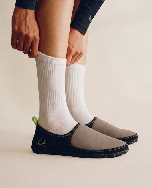 Person wearing lightweight mocha slip-on shoes with white socks on a neutral background