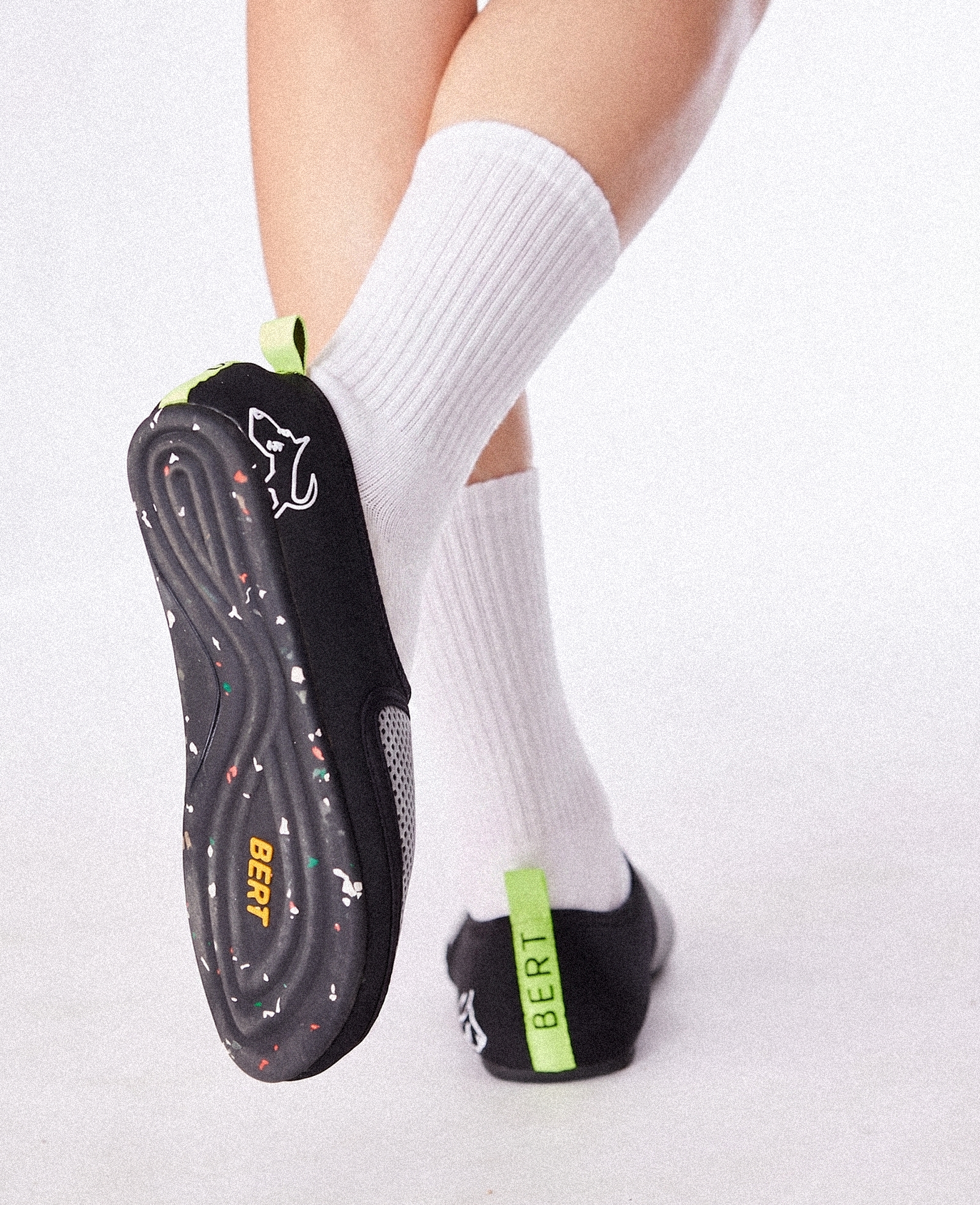 Black slip-on lightweight shoe with white sole speckles, neon heel tab, and white socks