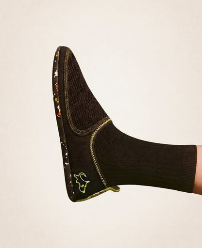 Black slip-on shoe with yellow stitching, mesh upper, and patterned sole on foot