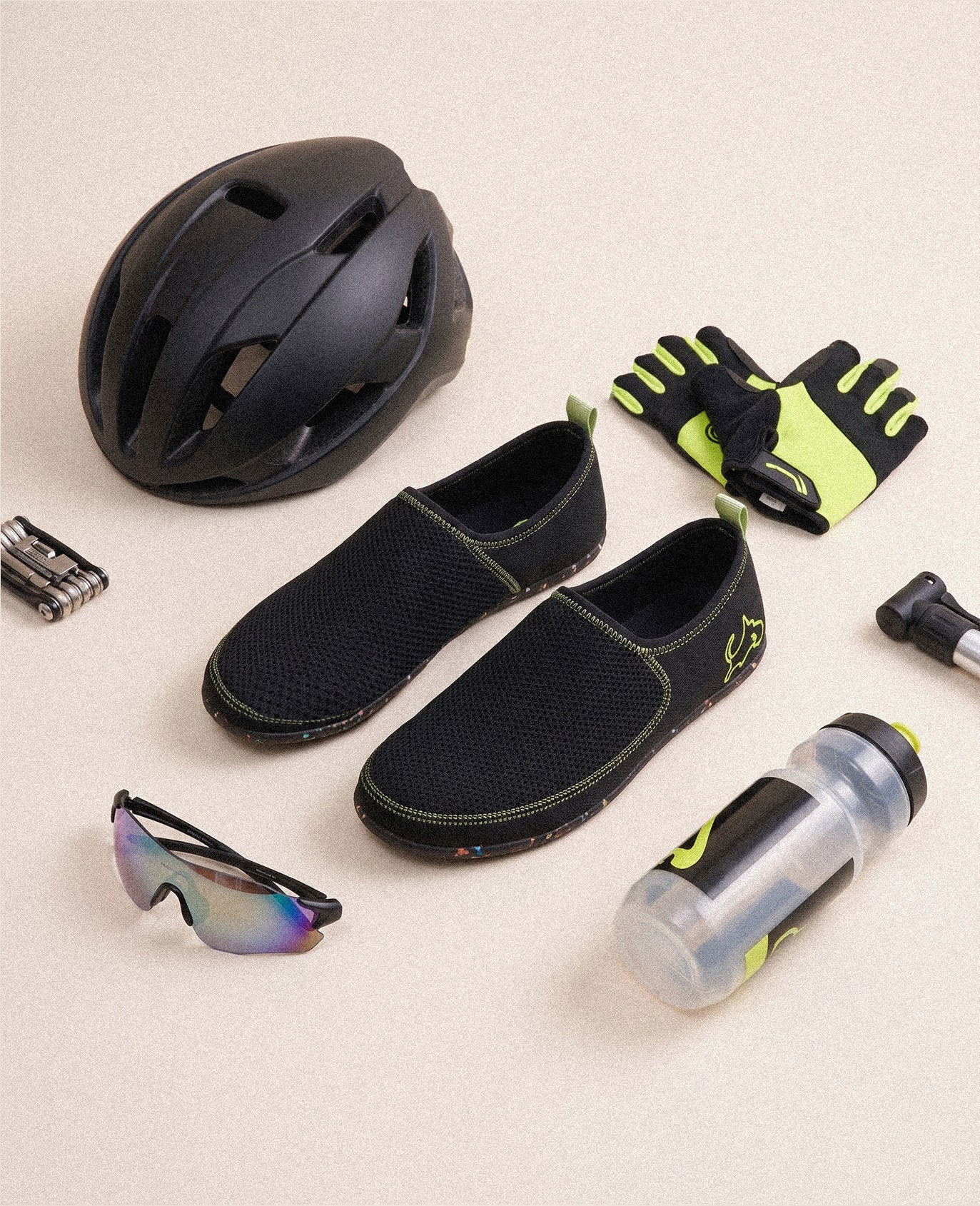 Black slip-on athletic shoes with mesh design, shown with cycling gear on beige background