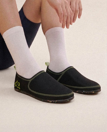 Black slip-on lightweight shoes with neon accents and white socks, worn by a seated person.