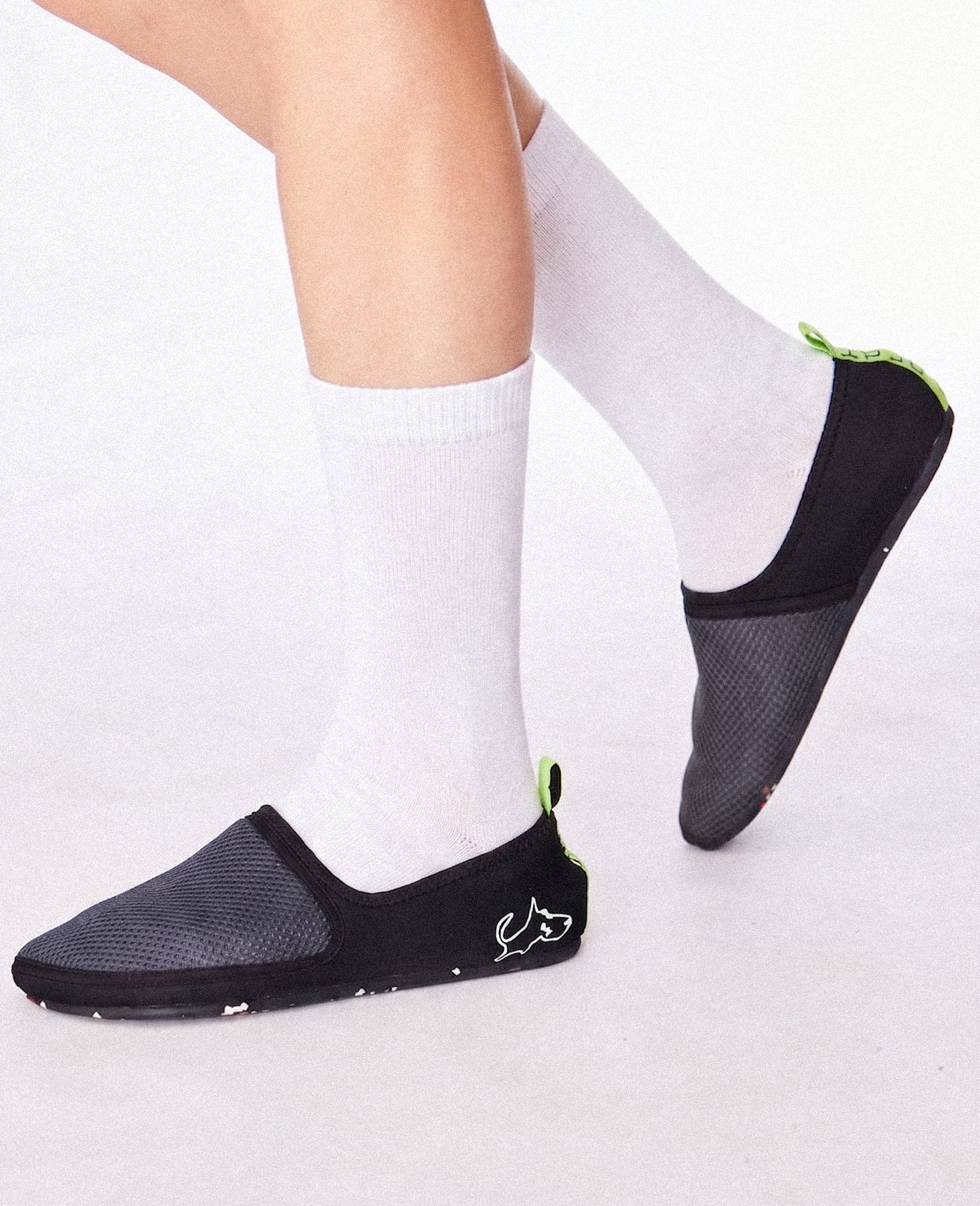 Lightweight black slip-on shoes with mesh upper, white socks, neon green accents, minimalist design.