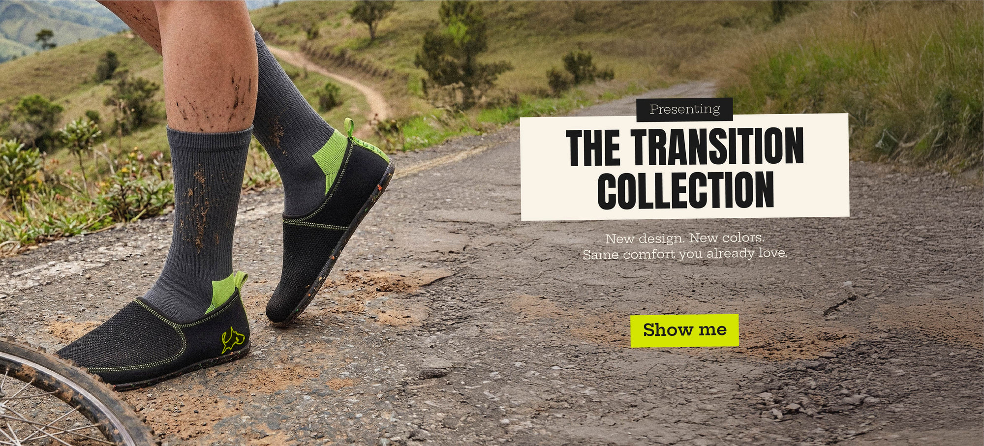 Lightweight black slip-on shoes with green accents worn outdoors on a muddy trail, bicycle wheel visible.