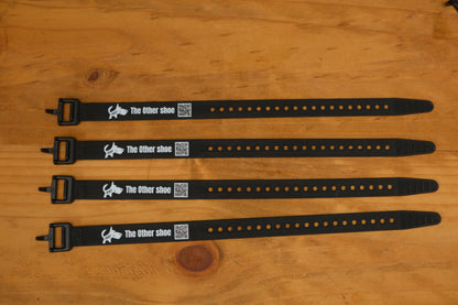 Four black adjustable shoe straps labeled 'The Other shoe' with QR codes on a wooden surface.
