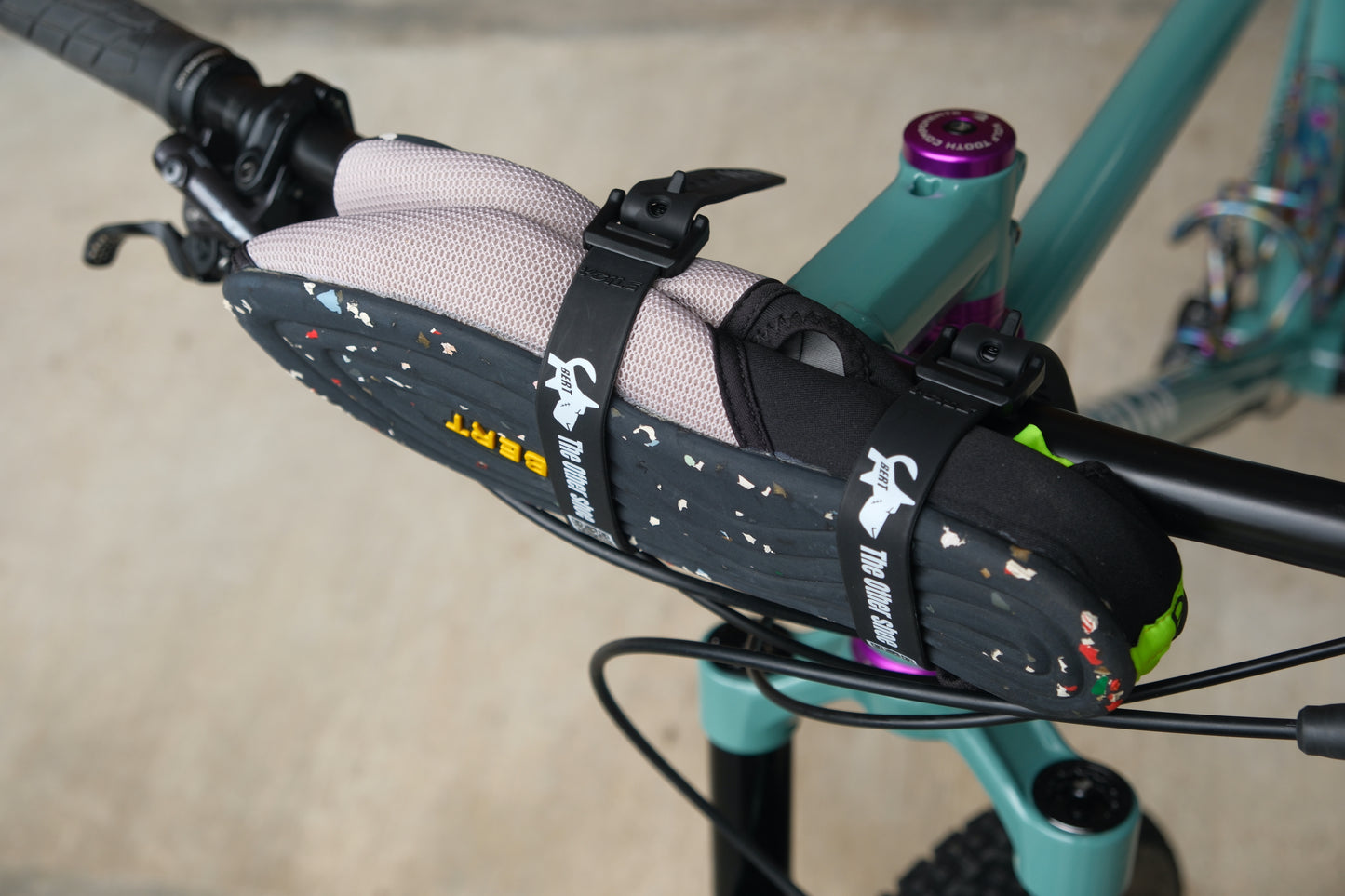 Lightweight slip-on shoes strapped to a teal bicycle handlebar with black straps